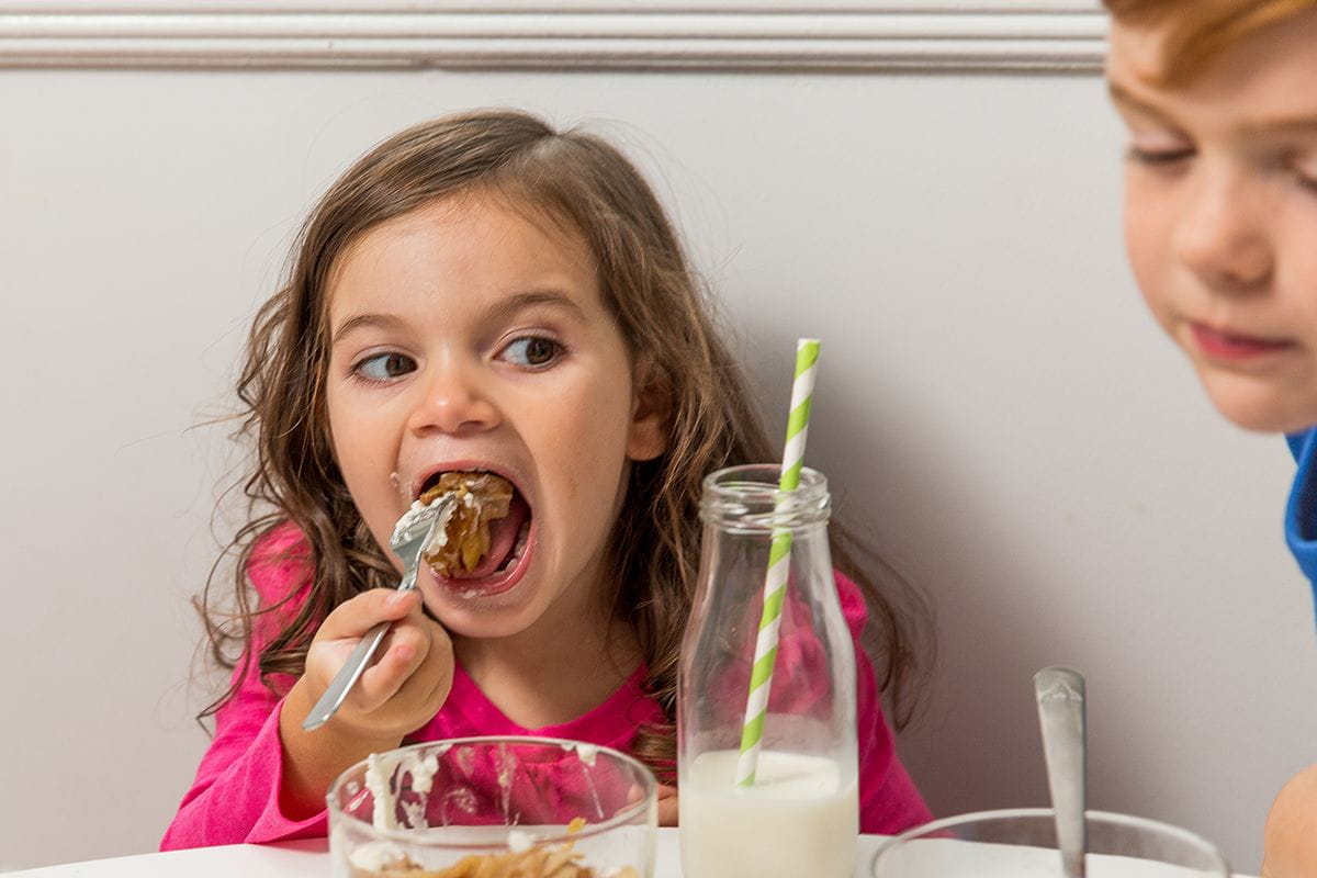 girl biting into apple crisp on fork milk bottle